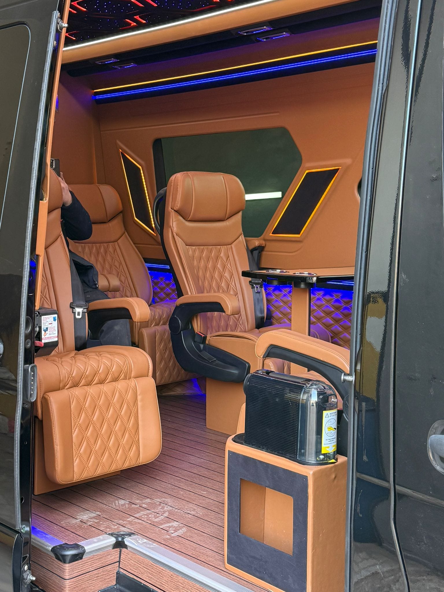 Mercedes Sprinter Innenraum mit offener Schiebetür – Executive-Einzelsitze in cognacfarbenem Nappa-Leder mit Tisch und Bechern
