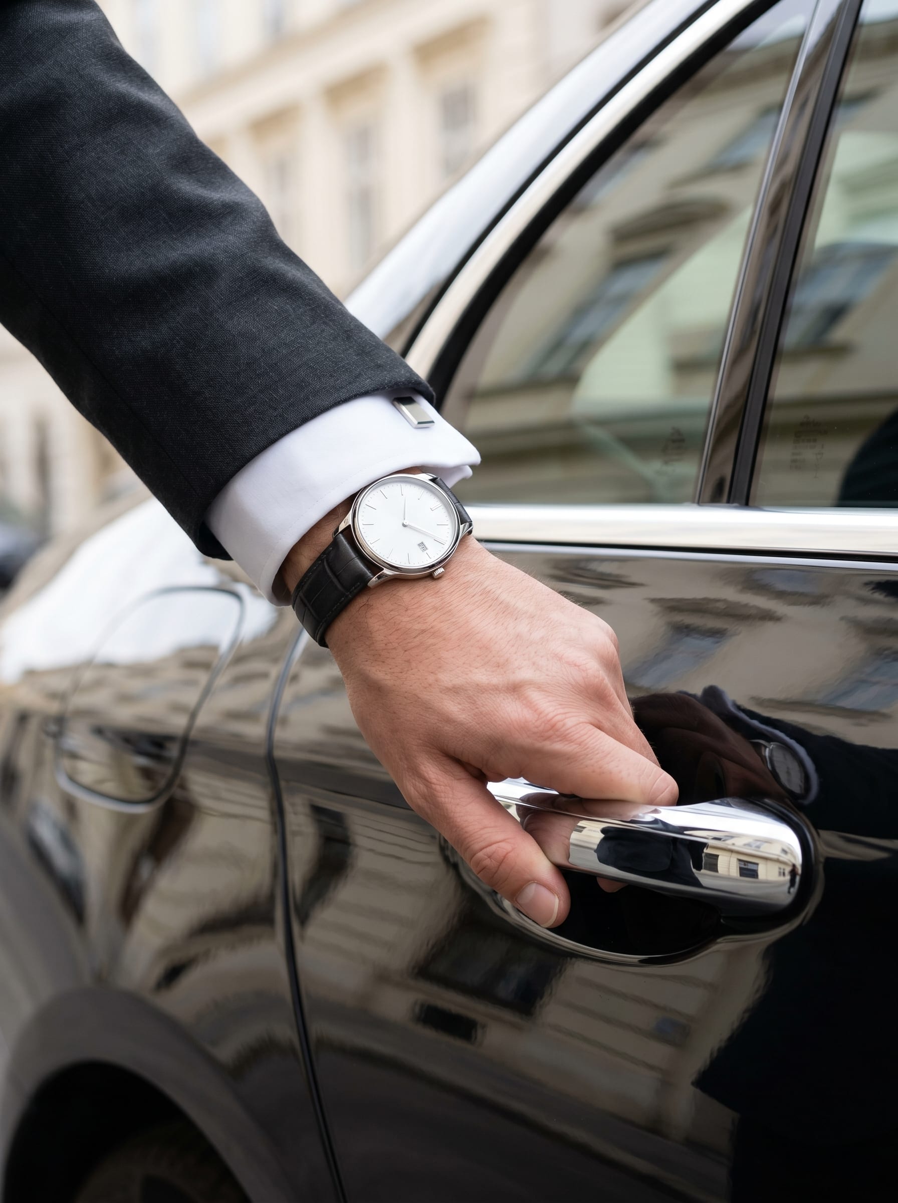 Nahaufnahme einer Chauffeur-Hand mit edler Armbanduhr und weißer Hemdmanschette an der Türklinke einer schwarzen Mercedes Limousine